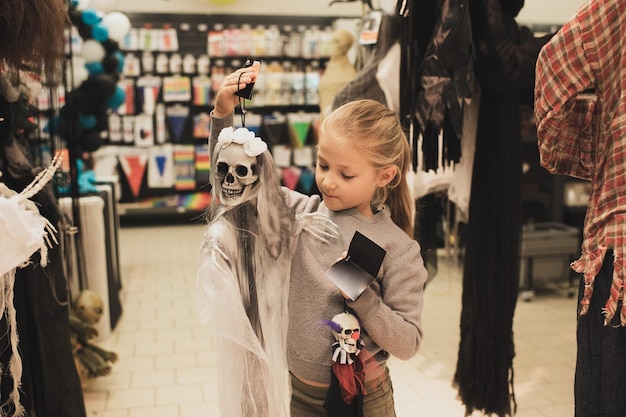 Una niña elige un esqueleto de juguete en una tienda para halloween