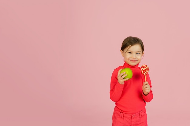 La niña elige entre una piruleta y una manzana verde. El concepto de nutrición adecuada.