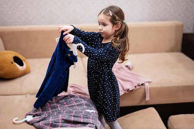 Niña eligiendo ropa del armario en casa en el sofá