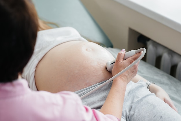 Una niña embarazada está teniendo un ultrasonido del abdomen en la clínica en primer plano. Examen medico