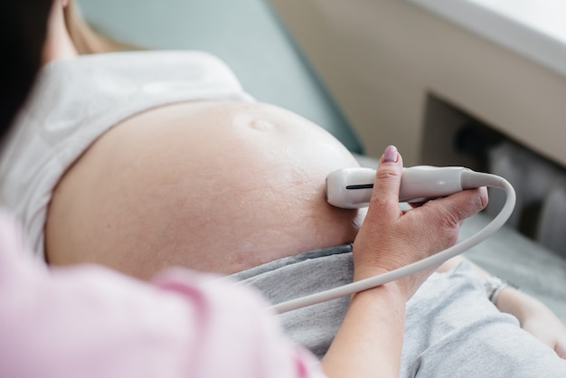 Una niña embarazada está teniendo un ultrasonido del abdomen en la clínica en primer plano. Examen medico