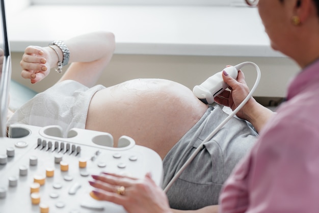 Una niña embarazada está teniendo un ultrasonido del abdomen en la clínica en primer plano. Examen medico.