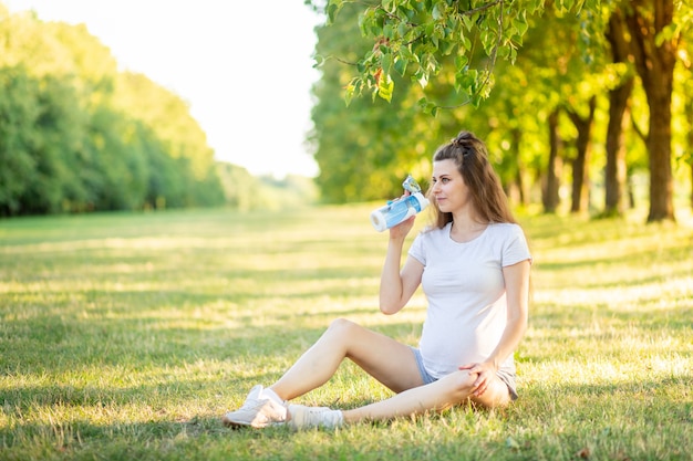 Una niña embarazada hace deportes en la naturaleza en el verano, yoga para mujeres embarazadas al aire libre.