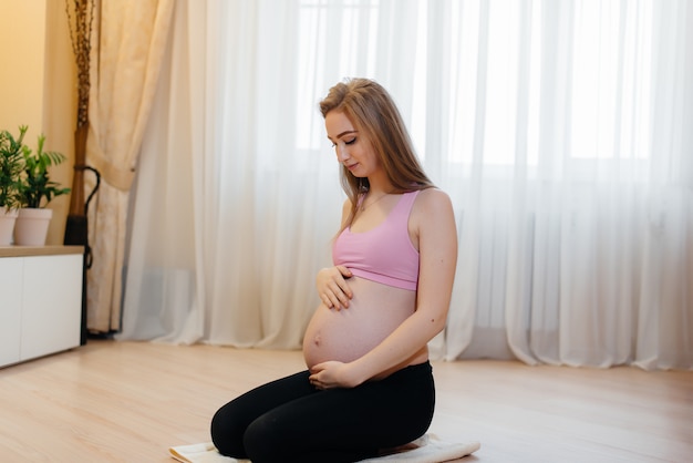 Una niña embarazada hace yoga en casa. Salud.