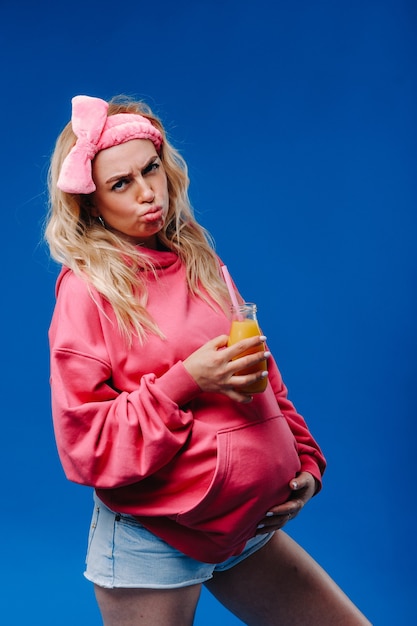 Niña embarazada en ropa rosa con una botella de jugo sobre un fondo azul.