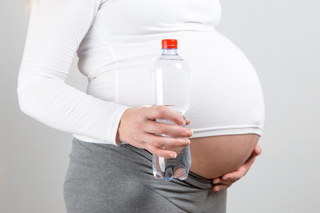 Una niña embarazada sostiene una botella de agua la importancia de una gran cantidad de líquido para la futura madre