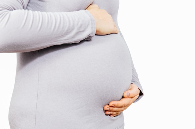 La niña embarazada sostiene un estómago con un vestido gris sobre un blanco