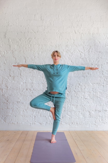 Niña embarazada en un traje deportivo azul se encuentra en pose de yoga, retrato de cuerpo entero