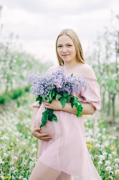 Niña embarazada con un vestido rosa en un jardín de flores sosteniendo una lila