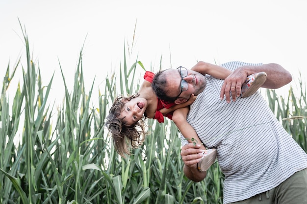 Foto niña emocionada con cabello rubio sentada en los hombros de su padre riendo en el campo de maíz
