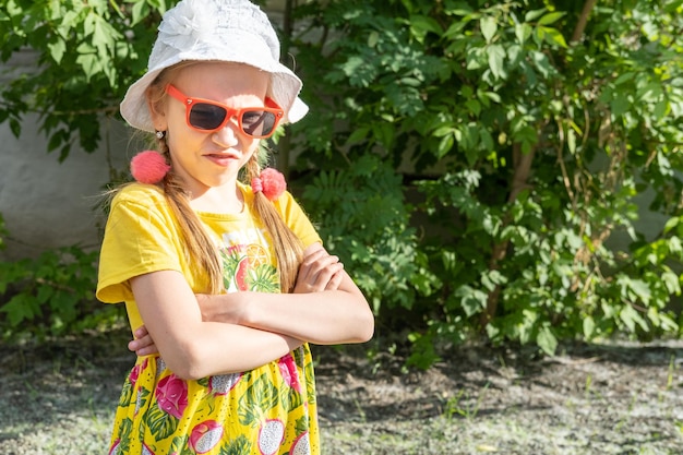 Una niña emocional frustrada con un vestido amarillo brillante, un sombrero blanco y gafas de sol arrugó la nariz