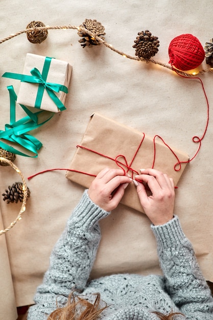 Una niña empaca un libro como regalo, lo envuelve en papel artesanal y lo venda con una cuerda roja. Regalos de Navidad y año nuevo para las vacaciones.