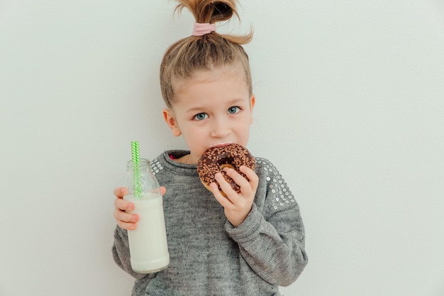 Una niña encantadora está comiendo donas de chocolate con una botella de leche