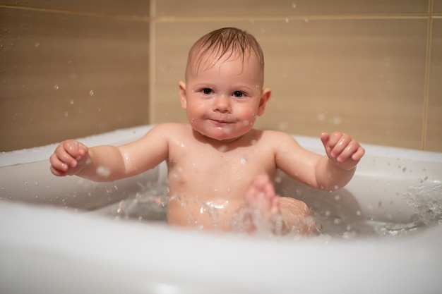 Niña encantadora juega en el agua en una pequeña piscina inflable para bebés ubicada en la ducha en el baño, niña sonriendo y divirtiéndose