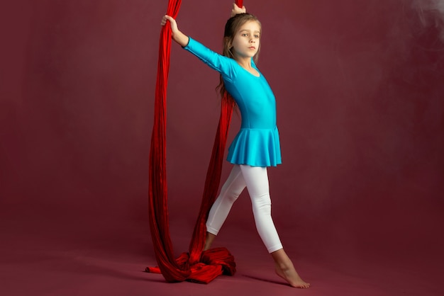 Niña encantadora en un traje de gimnasia azul preparada para la actuación con una cinta roja y aireada