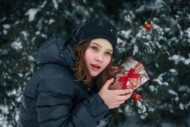 La niña encontró un regalo debajo del árbol y representa lo que hay dentro de la caja. Un niño con un don. Año nuevo. Una caja con un regalo para Navidad.