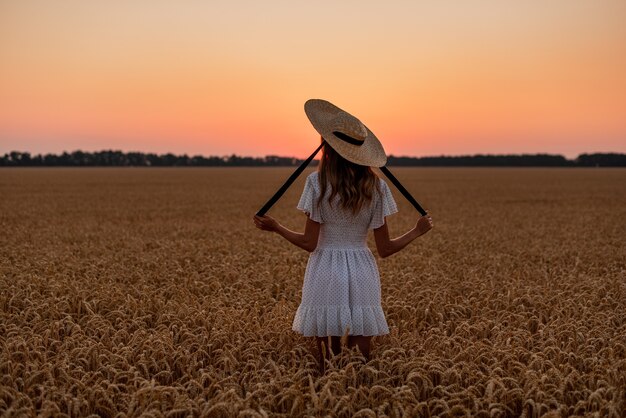 la niña se encuentra con el amanecer en un campo de trigo en la cabeza es un sombrero de paja con cintas