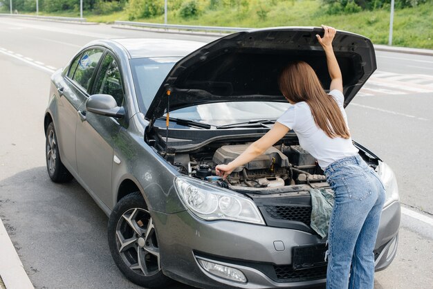 Una niña se encuentra cerca de un automóvil averiado en medio de la carretera y mira debajo del capó. Avería y avería del coche. Esperando ayuda.