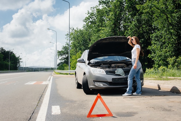 Una niña se encuentra cerca de un automóvil averiado en medio de la carretera y mira debajo del capó. Avería y avería del coche. Esperando ayuda.