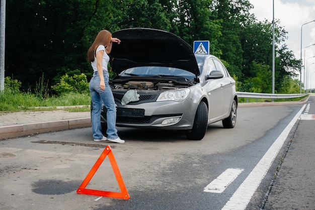 Una niña se encuentra cerca de un automóvil averiado en medio de la carretera y mira debajo del capó. Avería y avería del coche. Esperando ayuda.