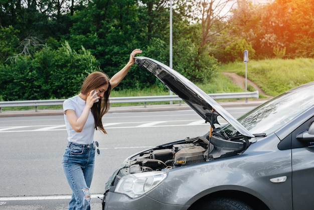 Una niña se encuentra cerca de un automóvil averiado en medio de la carretera y pide ayuda por teléfono.