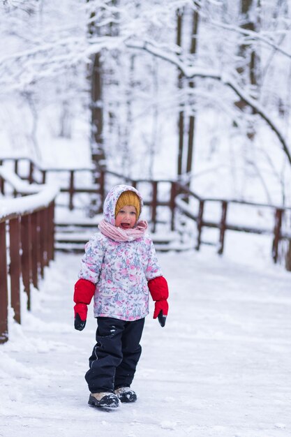 Una niña se encuentra cerca de la barandilla en el bosque de invierno.