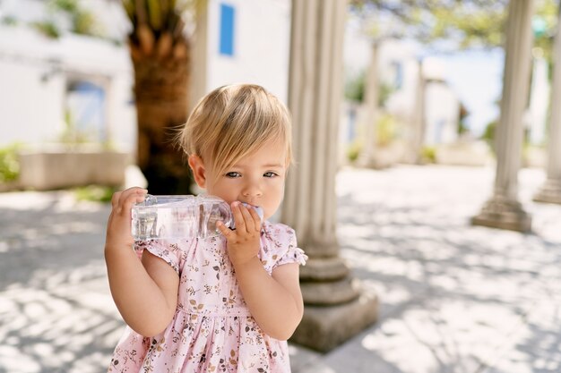 Niña se encuentra cerca de una columna y roe una botella de agua