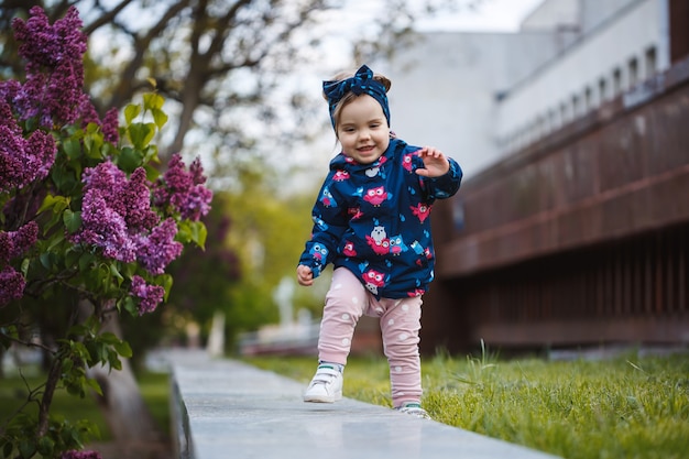 Una niña se encuentra cerca de un exuberante arbusto de lilas, sonríe y huele flores de color púrpura