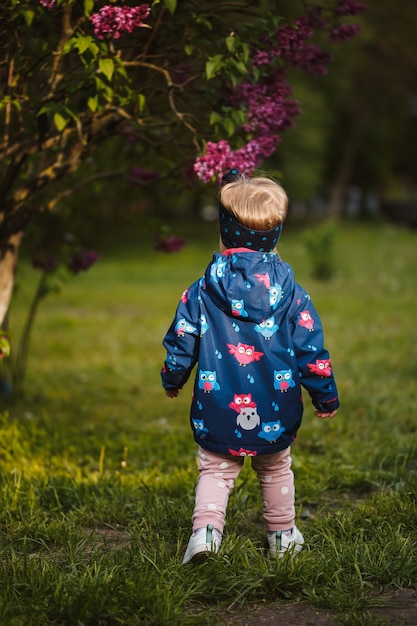 Una niña se encuentra cerca de un exuberante arbusto de lilas, sonríe y huele flores de color púrpura