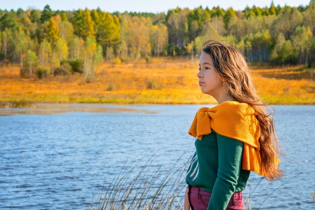 Una niña se encuentra cerca del lago La niña mira la naturaleza otoñal Los colores del bosque otoñal y la niña