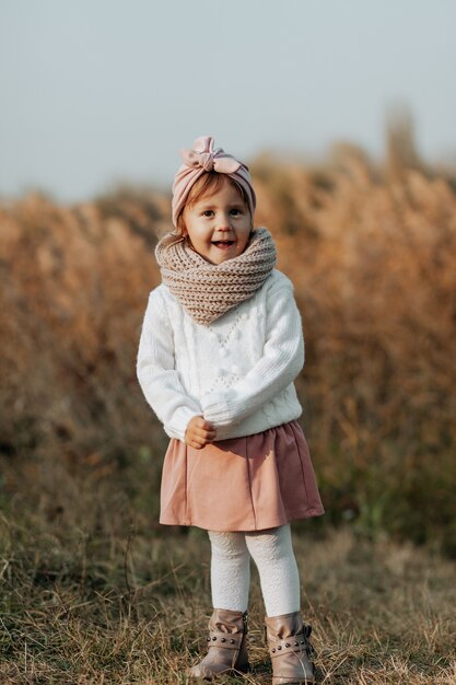 Una niña se encuentra en un claro. Otoño de oro. el niño está parado en el césped con un suéter de punto blanco y sosteniendo un juguete suave