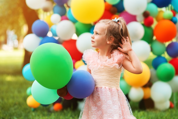 Una niña se encuentra en el contexto de globos de colores y mira hacia otro lado.