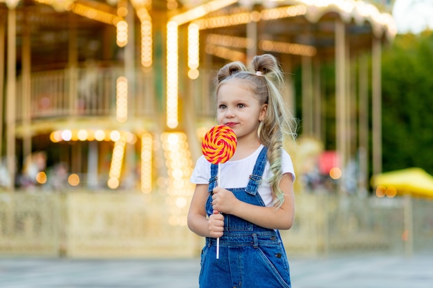 Una niña se encuentra en un parque de atracciones con una paleta grande.