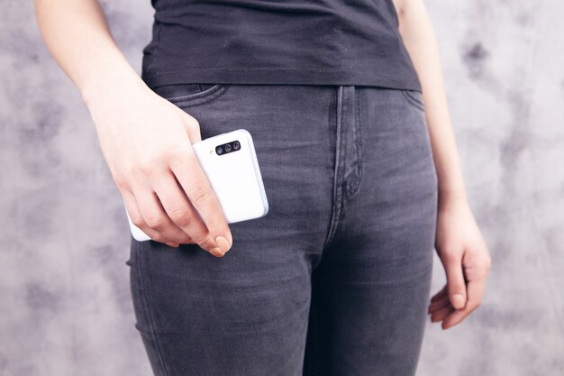 Una niña se encuentra con un teléfono en sus manos sobre un fondo gris