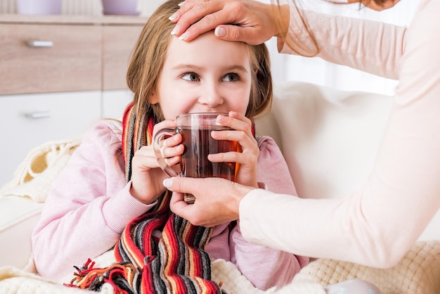 Niña enferma en bufanda bebiendo té