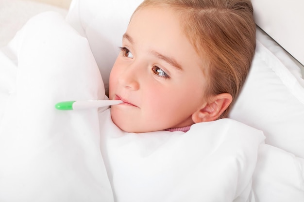 Niña enferma descansando en la cama con fiebre midiendo la temperatura con