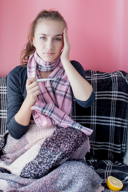 Niña enferma con fiebre comprobando el termómetro de mercurio sobre fondo rosa