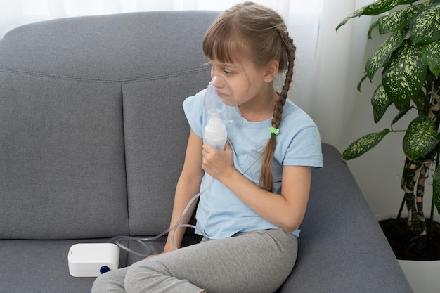 la niña enferma inhala sobre fondo gris con espacio para copiar. Chica haciendo inhalación con nebulizador en casa. niño asma inhalador inhalación nebulizador vapor enfermos tos.