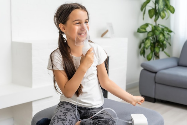 la niña enferma inhala sobre fondo gris con espacio para copiar. Chica haciendo inhalación con nebulizador en casa. niño asma inhalador inhalación nebulizador vapor enfermos tos.