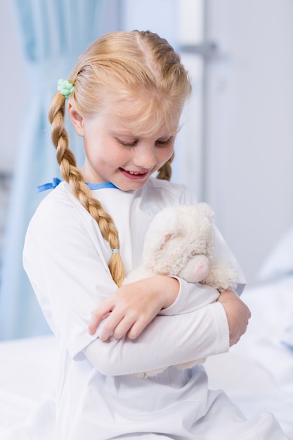 Niña enferma con osito en cama de hospital