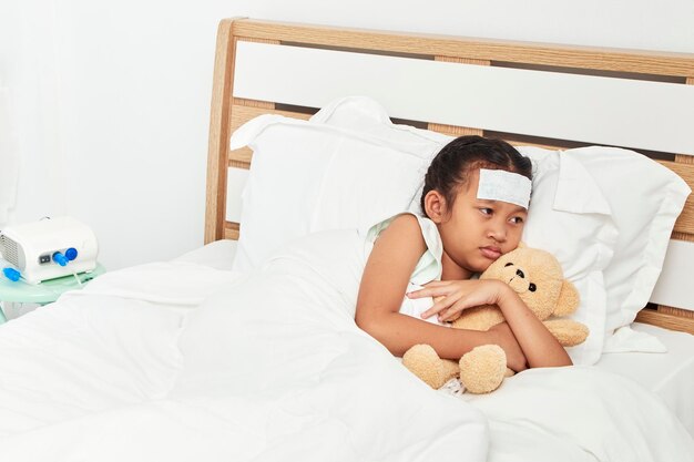 Foto niña enferma con un oso de peluche tendido en la cama