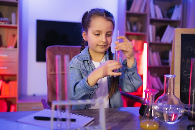 Foto niña enfocada haciendo un experimento de química mirando un tubo de ensayo en la sala de estar