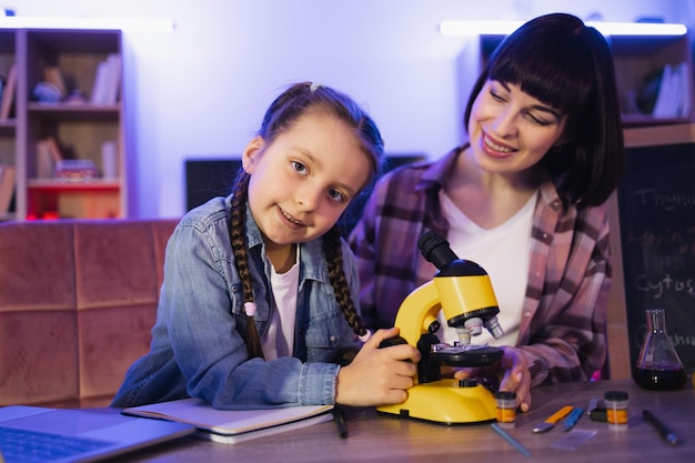 Niña enfocada mirando la cámara trabajando con el microscopio electrónico