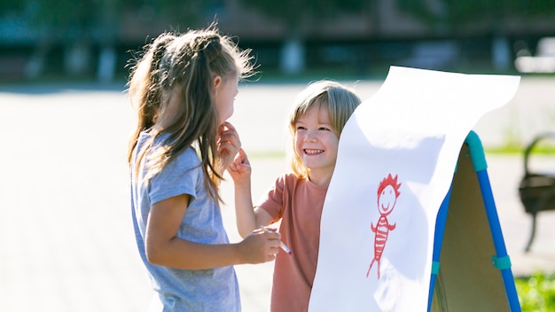 Niña enseña a un niño a dibujar sobre papel.