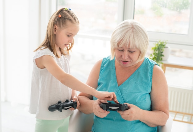 Niña enseñando a la abuela a jugar con el joystick