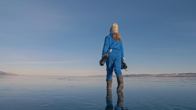 La niña entrena en patinaje de velocidad sobre hielo El niño patina en invierno con gafas deportivas azules Sosteniendo patines en las manos preparándose para comenzar