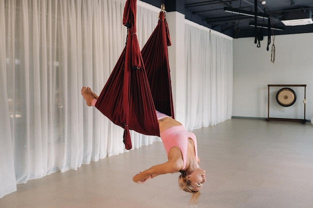 Una nina un entrenador de aero yoga esta colgado en una hamaca en el salon del club de yoga una mujer con ropa deportiva rosa esta haciendo yoga antigravedad. Foto Premium