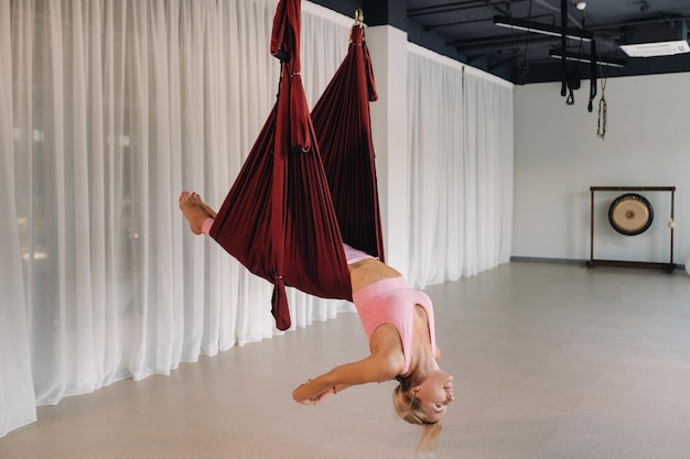 Una niña, un entrenador de aero yoga, está colgado en una hamaca en el salón del club de yoga, una mujer con ropa deportiva rosa está haciendo yoga antigravedad.