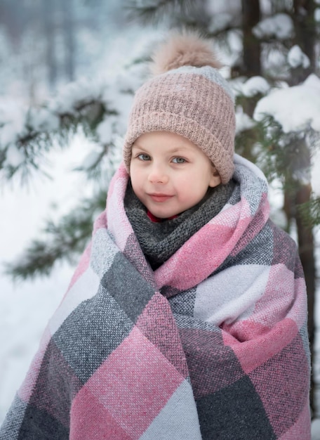 Niña envuelta en una manta en el bosque de invierno