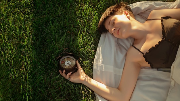 Una niña envuelta en una manta yace en la hierba verde junto a un despertador que promueve un sueño saludable